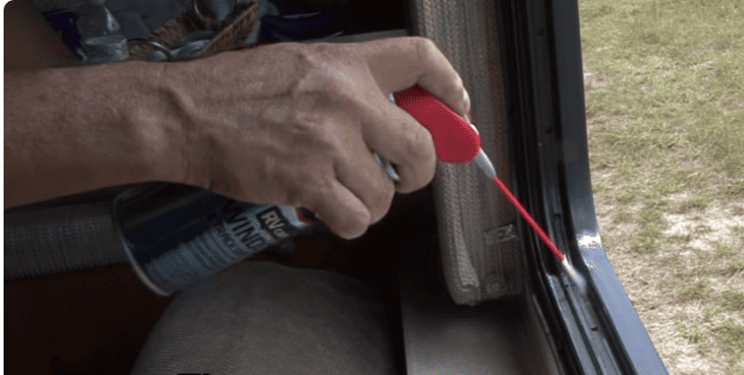 A person's hands applying WD-40 lubricant to the track of an RV window.